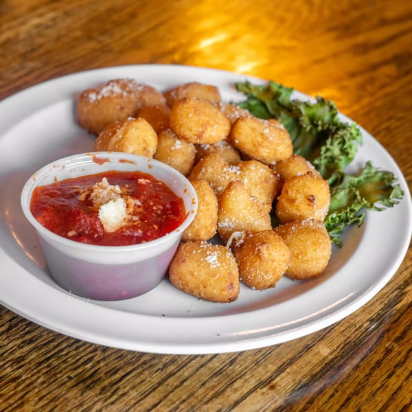 Golden-fried cheese curds with marinara sauce and lettuce on a white plate.