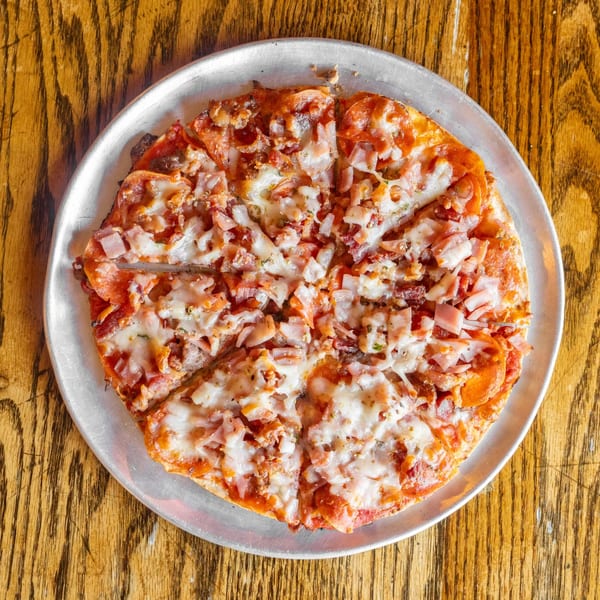 A freshly baked, sliced pizza with pepperoni, ham, and melted cheese on a metal pan.