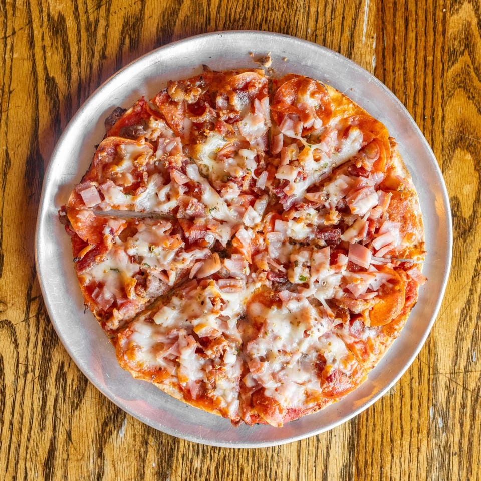 A freshly baked, sliced pizza with pepperoni, ham, and melted cheese on a metal pan.