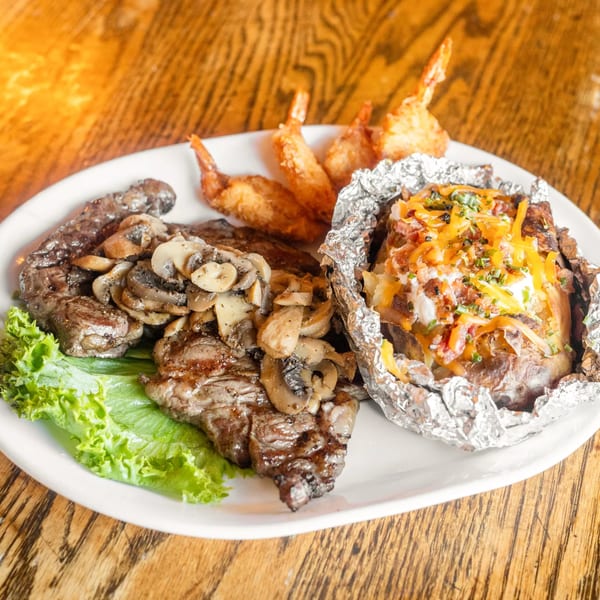 Marquarts Landing Inc. bar-&-grill steak with mushrooms, baked potato, and fried shrimp on a white plate.