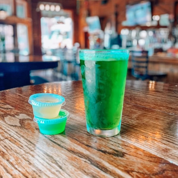 A vibrant green drink and two small cups of yellow and green liquid on a wooden table.
