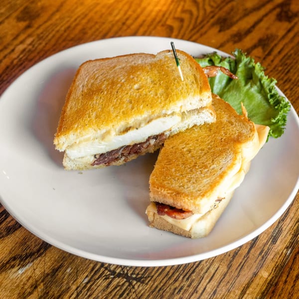 Grilled sandwich with melted cheese and meat, served with lettuce on a white plate.