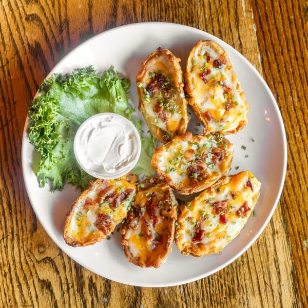 A plate of potato skins topped with melted cheese, bacon, and chives, served with sour cream and lettuce.