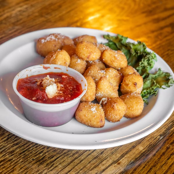 Golden fried cheese curds with marinara sauce and lettuce on a white plate.
