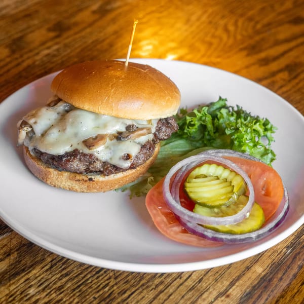 Mushroom Swiss burger with lettuce, tomato, onion, and pickles on a white plate at Marquarts Landing.