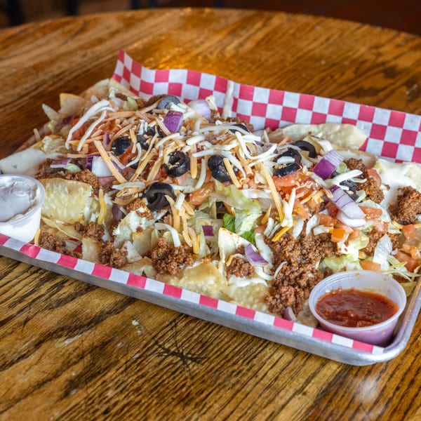 Loaded nachos with ground beef, cheese, olives, lettuce, and tomatoes, served with sour cream and salsa.