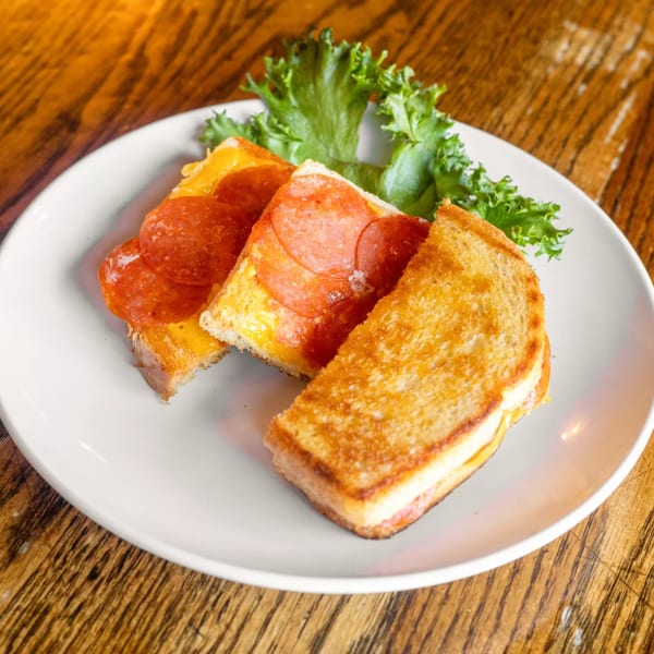 Grilled cheese sandwiches with pepperoni and melted cheese, garnished with lettuce on a white plate.